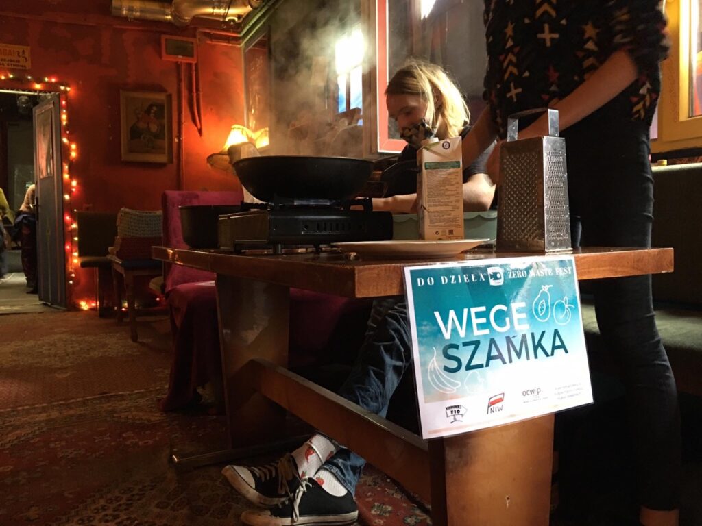 ciemna sala, a w niej przy stoliku młodzi ludzie gotują wegańskie potrawy