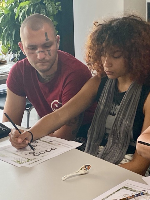 dziewczyna rysuje kwiaty ze wzoru, obok siedzi mężczyzna i patrzy co ona robi