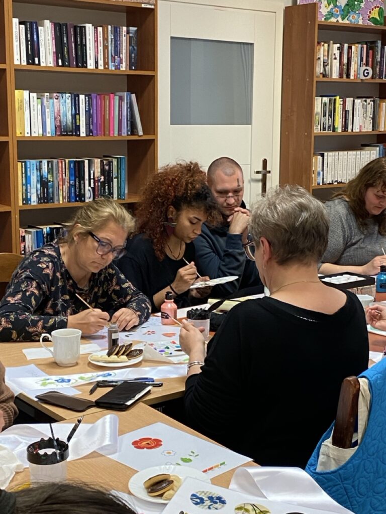 grupa osób przy stołach zastawionych materiałami kreatwnymi