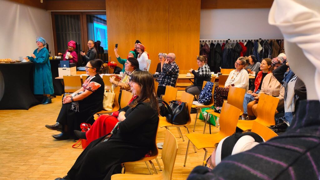 widowni, a w tle grupa kobiet w turbanach z chust