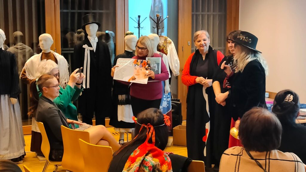 kobiety stoją na scenie, jedna z nich pokazuje na planszę