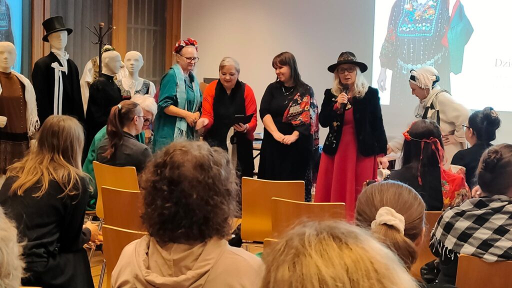 Grupa kobiet w kolorowych strojach stoi przed widownią. Widać teżmaneki ny ubrane w stroje ludowe z opolszczyzny