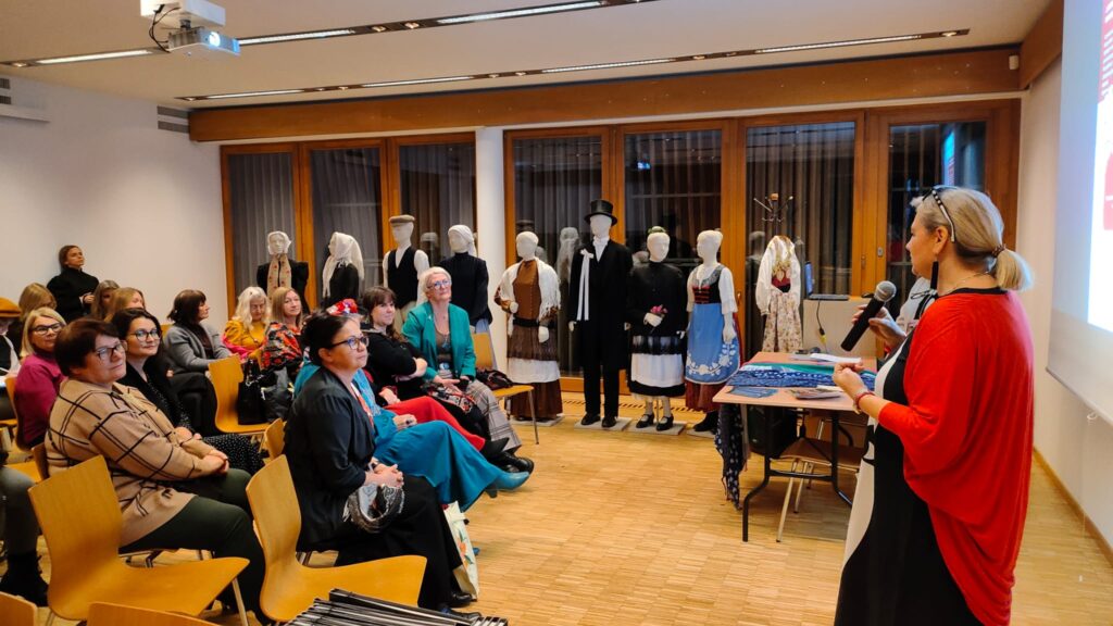 widownia pełna kobiet, na xcenie stoi kobieta ubrana w czerwoną, powłóczystą sukienkę