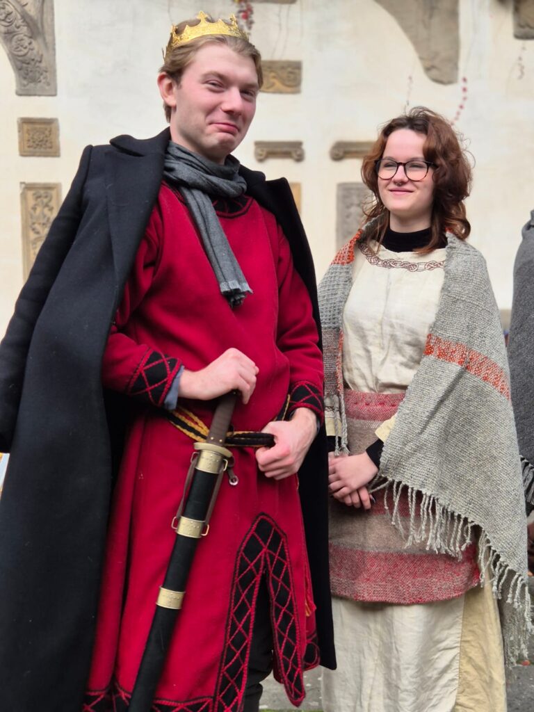 mężczyzna z w czerwonym kubraku i czarnej pelerynie, z korona na głowie stoi z kobietą w białej sukni z fartuchem szarym i szarej chuście zarzuconej na ramiona
