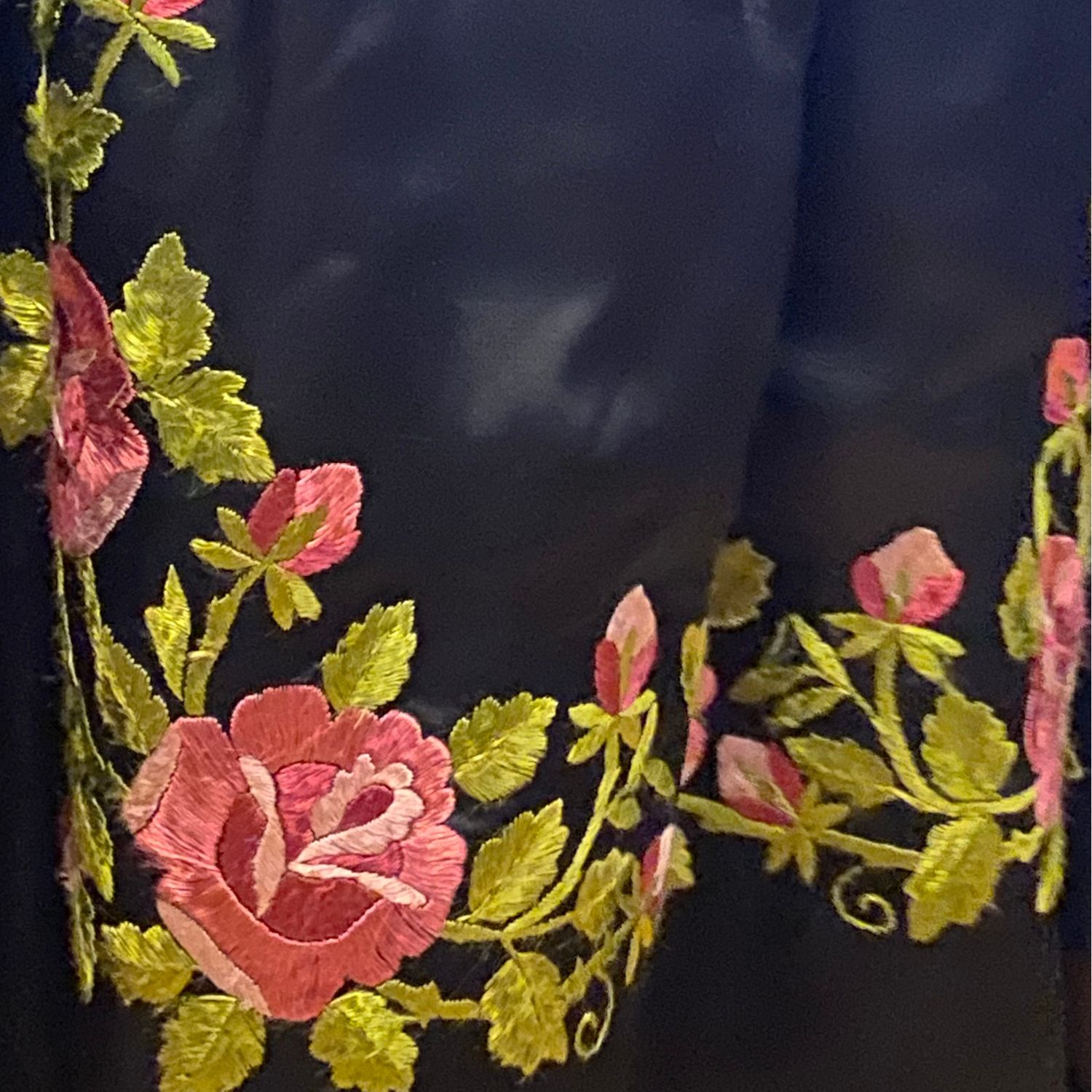 fragment czarnego fartucha śląskiego z narożnym haftem wykonanym jedwabnymi nićmi. Haft przedstawia motyw róż na zielonej łodydze.