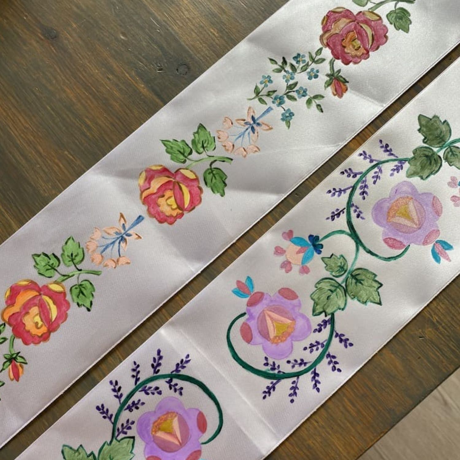 białe wstążki leżą na stole, pomalowane w kolorowe kwiaty ludowe