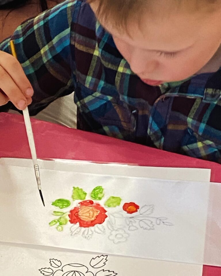 mały chłopiec maluje ludowy motyw śląskiej róży na białej wstążce