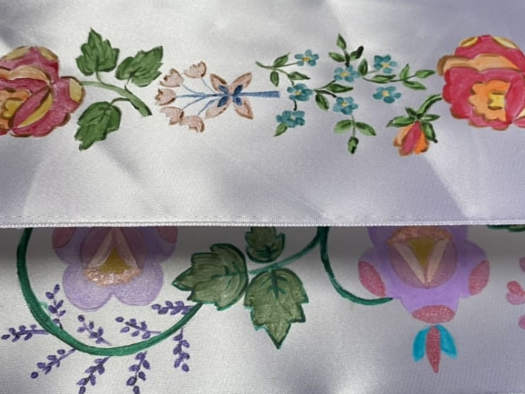 dwie białe wstążki z namalowanymi ręcznie ludowymi wzorami