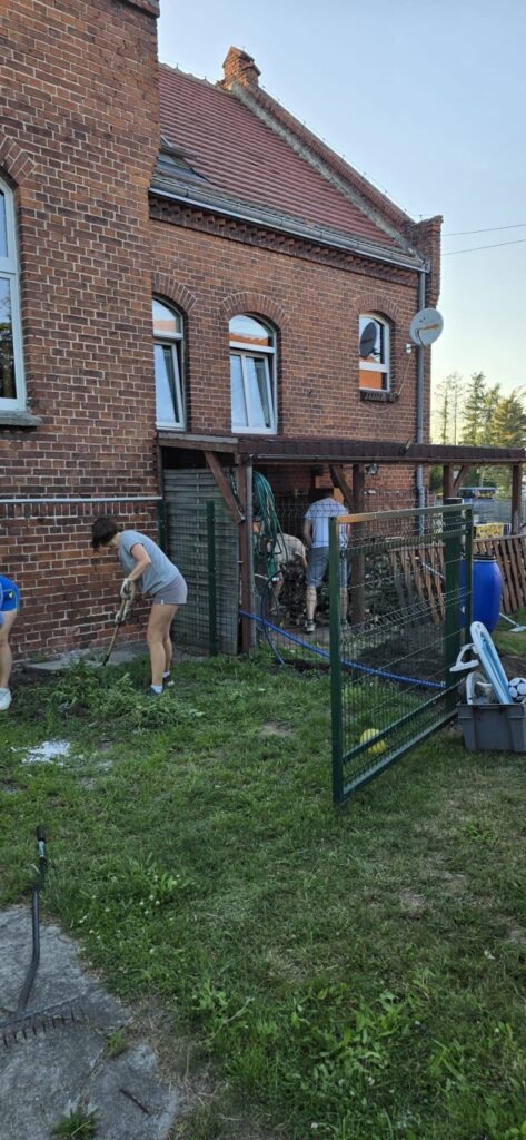 Mieszkańcy Lędzin usuwają chwasty i porządkują teren wokół budynku, który będzie służył lokalnej społeczności jako miejsce spotkań.