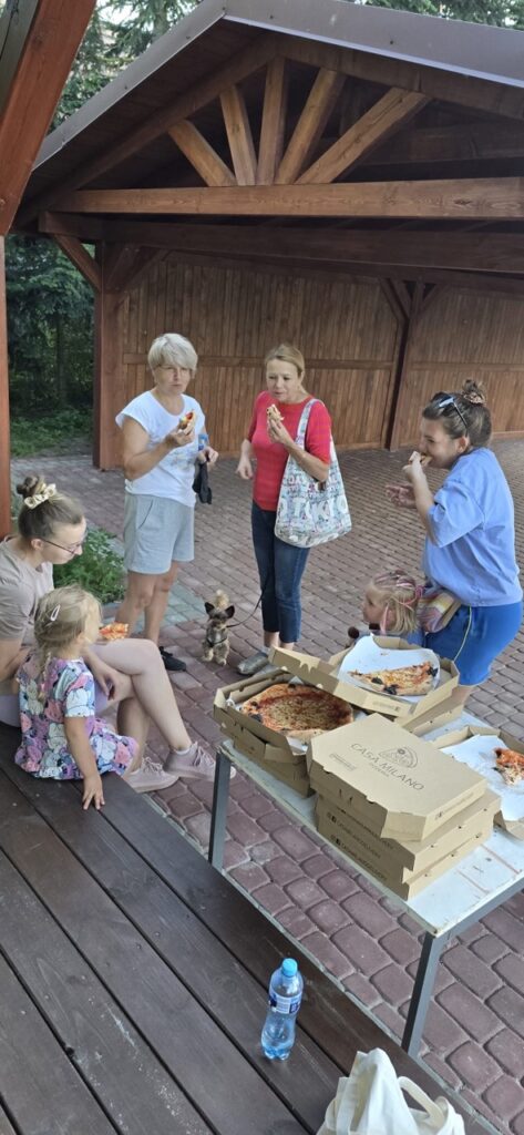 Uczestnicy akcji społecznej w Lędzinach odpoczywają przy wspólnym poczęstunku pizzą po zakończeniu prac porządkowych wokół nowej przestrzeni dla mieszkańców.