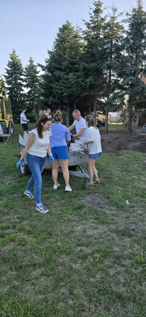 Mieszkańcy wspólnie wynoszą odpady na przyczepę podczas prac społecznych związanych z przygotowaniem nowego miejsca spotkań w Lędzinach.