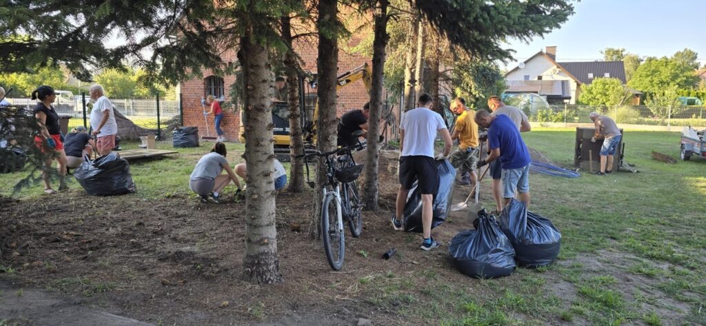 Szeroki widok na mieszkańców wspólnie porządkujących teren, zbierających odpady i przygotowujących przestrzeń do działań społecznych w Lędzinach.