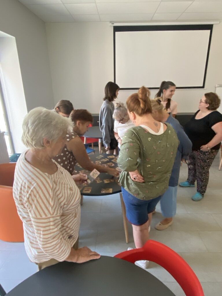 Kilka kobiet podczas warsztaów wybiera karty intuicyjne ze stolika. Dwie z nich rozmawiają.