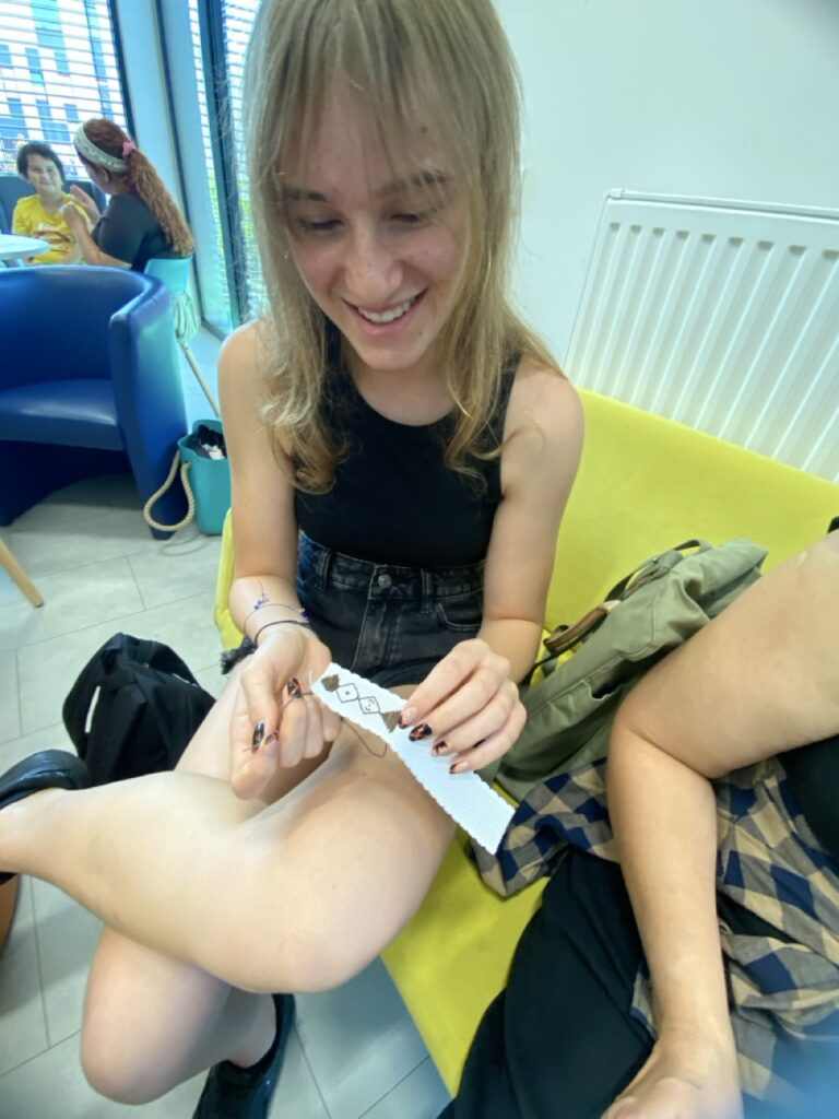 kobieta wyszywa na pasku kanwy - pokazuje swoja pracę z geometrycznymi wzorami