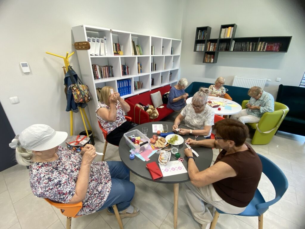 kobiety siedzą przy stolikach i wyszywają na pasku kanwy