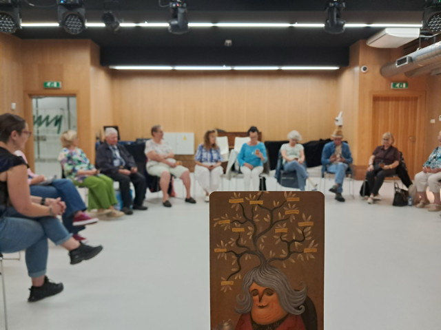 Grupa seniorów, na podstawie kart intuicyjnych opowiada czym dla nich jest muzyka i jaką pełni rolę w ich życiu. Pracuje nad opracowaniem idealnej oferty dla grupy podobnej do siebie. Prowadząca  siedzi w kręgu z resztą uczestników i uważnie słucha. Na pierwszym planie widać jedną z kart, wybrana przez uczestniczkę warsztatu