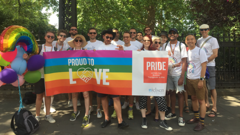 grupa osób stoi z tęczową flagą z napisem PRIDE TO LOVE
